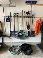 Wide view of all garden tools, snow shovels, broom and hose hanging on garage wall and on floor