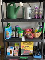 Full shelf showing all gardening items including watering cans on top, plant food and pest control sprays in middle, garbage bags and other boxes on bottom shelf.