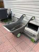 Side view of Keter Realbarrow garden cart showing the tub, handle grips, and wheels in outdoor setting.