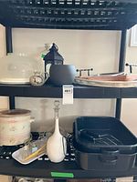 Shelf display showing crock pot, roasting pans, decorative jug, glass decanter, cake dome, utensils and black lantern