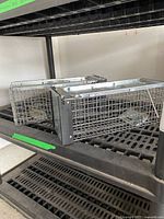 Two metal wire cage live traps placed on a black plastic shelving unit.