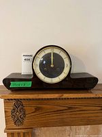Full frontal image of dark wood mantel clock with circular face and brass trim.