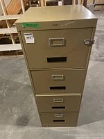 Front view of beige metal filing cabinet showing four drawers with label holders and locks. Condition shows wear and the bottom drawer lock is non-functional.