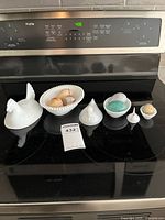 Three hen-shaped glass dishes with lids and six decorative eggs arranged on a black stovetop.