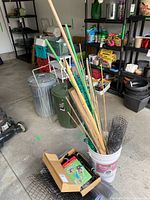 Full view showing plant stakes, wire mesh rolls, and boxes in bucket and nearby on floor in garage/storage area.