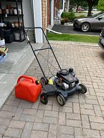 Photo showing full view of Remington push lawn mower, orange gas can, and oil bottle on paved driveway.