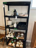Photo showing the black plastic shelf unit with various items on the shelves, providing scale and context for the shelf size and condition.