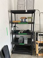 Full view of black plastic shelving unit with items placed on shelves (not included in sale). Shows the construction and condition of the shelf.