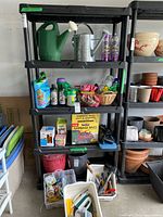 Front view of black plastic 5-tier shelf filled with various household items, used to show shelving unit structure and condition.