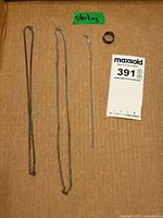 Three silver necklaces and one silver ring laid out on a cardboard surface with a 'sterling' label and maximum lot tag included.