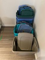 Stacks of various colored plastic storage bin lids and bins, arranged against wall on floor.