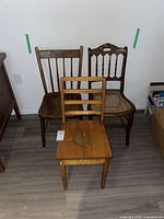 Photo showing three antique wooden chairs grouped together on a hardwood floor against a white wall, illustrating size and condition differences.