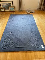 Full view of the blue carpet with visible carved border pattern placed on hardwood floor.