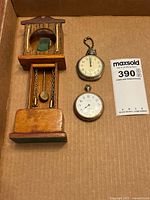 Top view photo showing the wooden pocket watch display stand and two vintage pocket watches laid flat in a box.