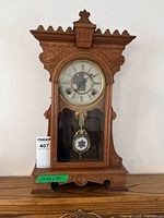 Full view of the Waterbury Clock Co. antique mantel clock with visible ornate wood carvings, glass front door, and pendulum.