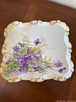 Full view of square ceramic tray with purple flower hand-painted design and gold trim on scalloped edges.