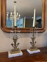 Pair of antique girandole ormolu urn candlesticks on marble bases with taper candles placed inside, shown in front of a mirror and chandelier reflection.