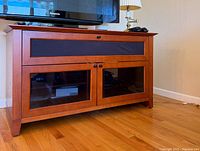 View of BDI Novia Series 8426 audio/video cabinet with a TV on top in a corner room setting on hardwood floor.