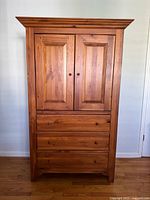 Front view of the full armoire showing two paneled doors and three drawers beneath with round knobs.