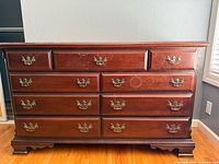 Front view of large wooden dresser showing nine drawers with ornate brass handles and bracket feet.