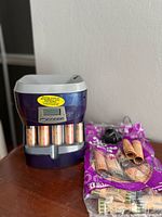 Front view of purple and gray Mag-Nif digital coin sorter with several rolls of brown coin sleeves and black power adapter placed next to it