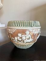 Photo of Roseville Donatello jardiniere vase showing detailed relief figures of cherubs and trees with multicolor glaze.