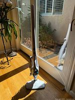 Upright PurSteam steam mop standing on hardwood floor near glass door, showing full unit.