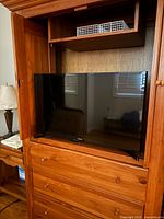 Samsung 32-inch LED TV placed in wooden entertainment cabinet, showing front screen and stand.