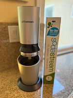 Front view of the silver SodaStream Crystal sparkling water maker with the CO2 carbonator box beside it on a kitchen counter.