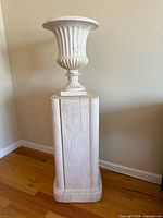 Full view of the terracotta urn on stone pedestal against wall showing overall structure and condition