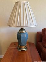 Full view of the vintage table lamp showing the blue ceramic base, brass footed base, and beige pleated lampshade.