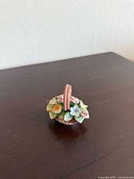 Front angle view showing mini flower basket with colorful flowers and brown handle on wood surface.
