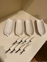 Four white ceramic dishes shaped like corn on the cob, placed side by side on a flat surface.