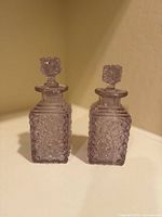 Front view of the pair of purple vintage crystal perfume bottles on a white surface.