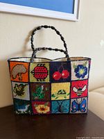 Front view of colorful patchwork needlepoint tote with various animals, insects, and flowers in squares.