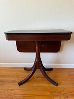 Front view of the rectangular mahogany flip top game table with turned pedestal base and tripod legs with brass feet caps.