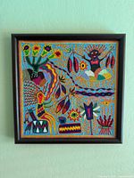 Full frontal view of square yarn painting in dark wooden frame hung on wall
