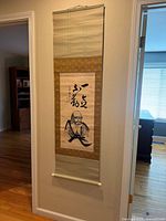 Full view of vintage Japanese hanging scroll on wall, shows entire scroll with patterned borders and hanging cord.