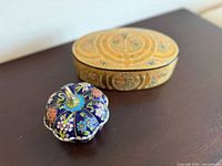 Oval hand-painted lacquer jewelry box featuring elaborate floral and geometric patterns alongside the cloisonne lidded pumpkin trinket box with colorful enamel flowers.