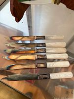Six vintage knives laid out flat showing mother of pearl handles and metal collars with aged blades