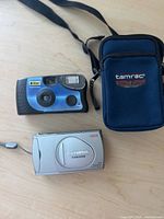 Top view showing Olympus CAMEDIA D-520 digital camera, blue point-and-shoot film camera, and blue Tamrac carrying case with shoulder strap.