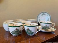 Front view of six cups with Christmas tree design and green rim, arranged on wooden surface.