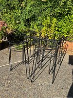 Four black tubular wire plant stands arranged outdoors, showing their round tops and tripod legs.