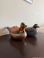 Two vintage hand painted wood lacquer duck figurines, hollow and openable as small boxes, shown side-by-side on a wooden surface.