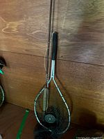 Full view of fly rod with reel attached and landing net leaning against wall