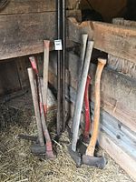 Group of axes, sledge hammers and pry bars leaning against wall
