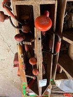 Wooden bin containing several similar red-handled braces; representative of included brace