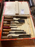 Open wooden case showing eight chisels of varying sizes and handles