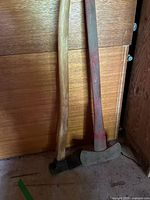 Splitting maul and double-bit axe leaning against wood panel