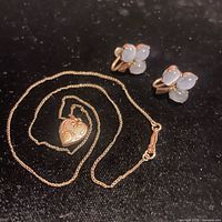 Heart pendant locket necklace and blue cat eye cabochon screwback earrings on black surface.